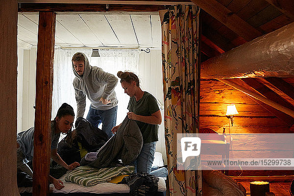 Weibliche und männliche Freunde falten Decken auf dem Bett in der Hütte