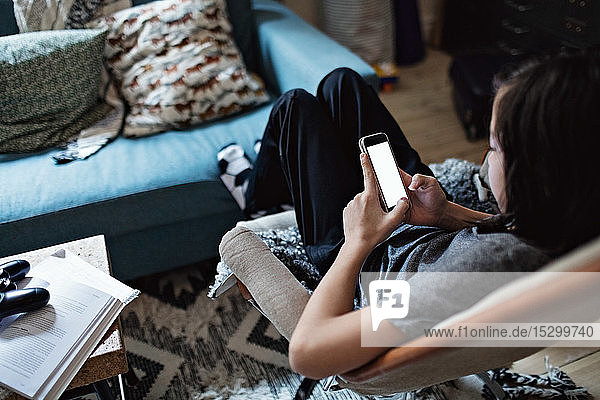 Schrägansicht eines Jungen  der ein Mobiltelefon benutzt  während er im Wohnzimmer sitzt
