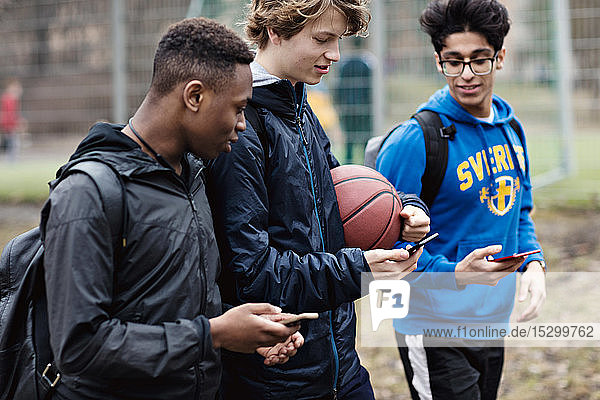 Freunde  die nach dem Basketballtraining auf der Straße mit Smartphones unterwegs sind