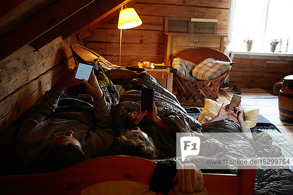 Hochwinkelansicht von Freundinnen und Freunden  die Smartphones benutzen  während sie in einer Hütte liegen