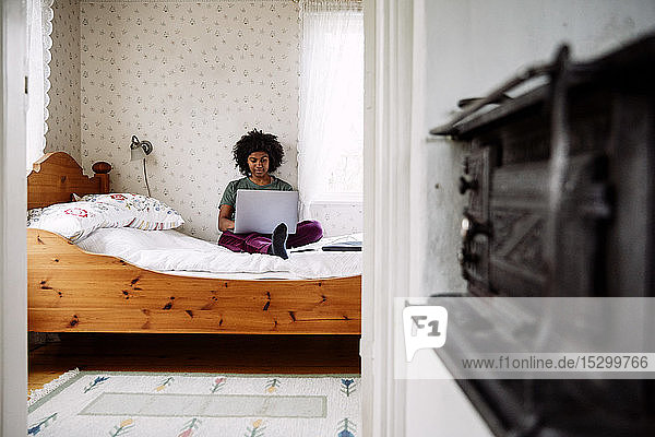 Junge Frau  die zu Hause am Laptop sitzt und sich im Bett entspannt  durch die Tür gesehen
