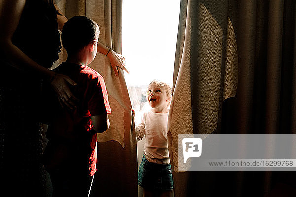 Mädchen steht am Fenster und schaut Mutter mit Junge im Hotelzimmer an