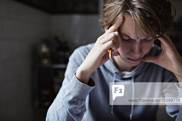 Gestresster Teenager mit dem Kopf in der Hand beim Lernen zu Hause