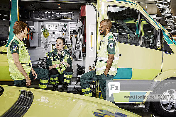 Männliche und weibliche Rettungssanitäter sprechen  während sie im Krankenwagen auf dem Parkplatz sitzen