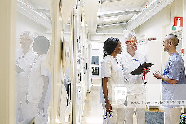 Lächelnde multiethnische Ärzte diskutieren stehend im Krankenhauskorridor