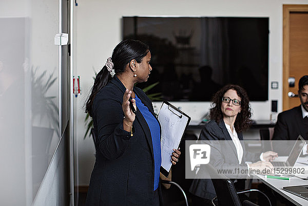 Businesswoman holding clipboard while discussing with colleagues during meeting in office