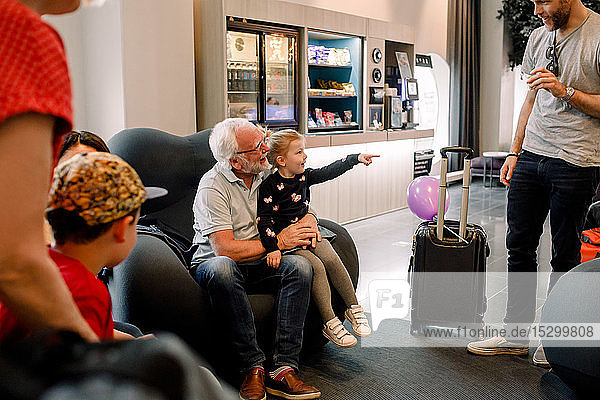 Lächelndes Mädchen spricht mit Vater  während es mit Großvater in der Lobby des Hotels sitzt
