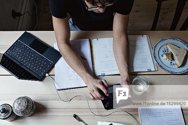 Hochwinkelansicht eines fleißigen jungen Mannes  der ein digitales Tablet benutzt  während er am Tisch Hausaufgaben macht