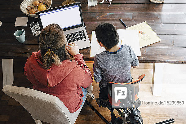 Hochwinkelansicht einer Mutter mit autistischem Sohn  die zu Hause sitzend ein Video auf einem Laptop anschaut