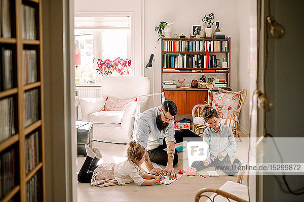 Father drawing with daughters while resting in living room at home