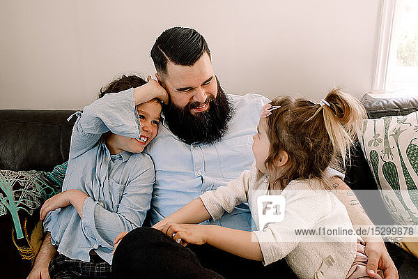 Glücklicher Vater spielt mit fröhlichen Töchtern  während er zu Hause auf dem Sofa sitzt