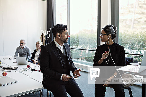 Geschäftsmann diskutiert mit Geschäftsfrau am Laptop mit Kollegen  die am Konferenztisch im Sitzungssaal arbeiten