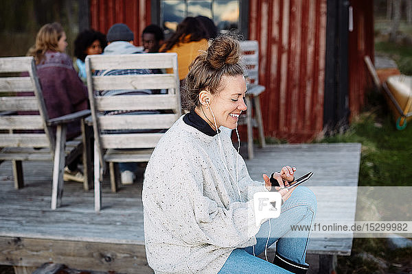 Smiling mid adult woman using smart phone while friends talking in background during sunset