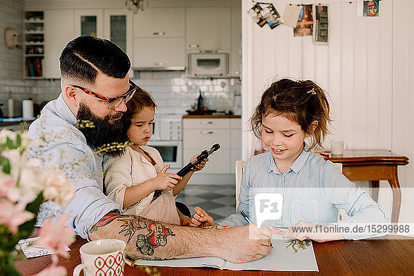 Vater hilft Mädchen bei den Hausaufgaben  während er mit Tochter am Esstisch sitzt