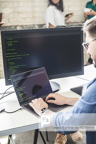 Männlicher Computerprogrammierer  der während der Arbeit am Schreibtisch im Büro in einem Laptop kodiert