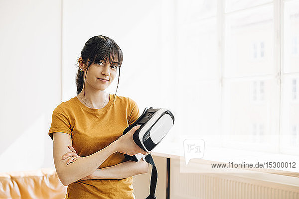 Portrait of female entrepreneur holding virtual reality simulator while standing by window