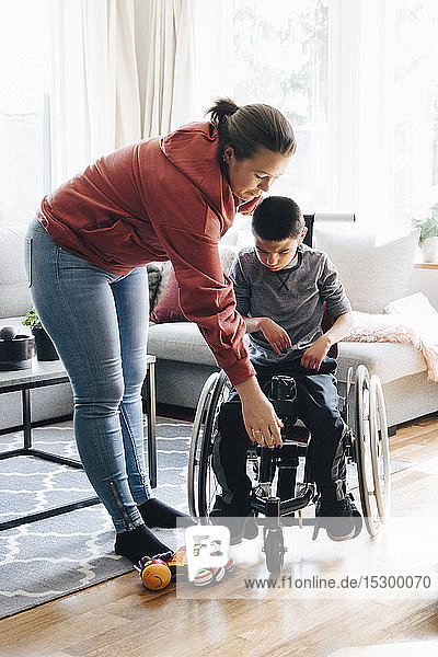 Mutter hilft autistischem Sohn  zu Hause auf motorisiertem Rollstuhl zu sitzen
