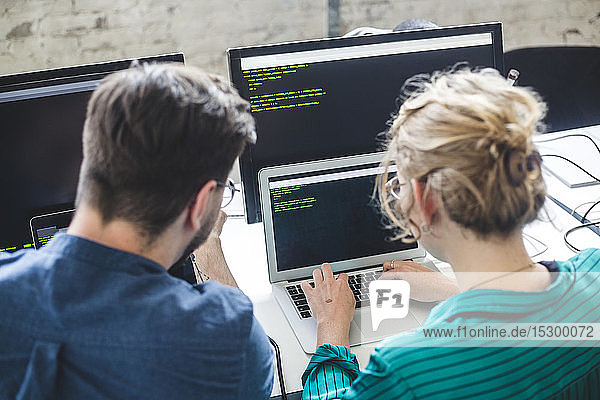 Rückansicht einer weiblichen IT-Expertin  die auf einem Laptop kodiert  während ein männlicher Hacker am Arbeitsplatz sitzt