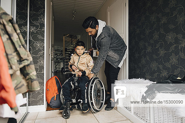 Vater schiebt autistischen Sohn im Rollstuhl sitzend auf dem Flur zu Hause