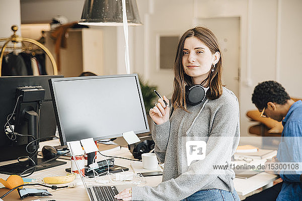 Porträt einer lächelnden Computerprogrammiererin mit Laptop am Schreibtisch im Büro