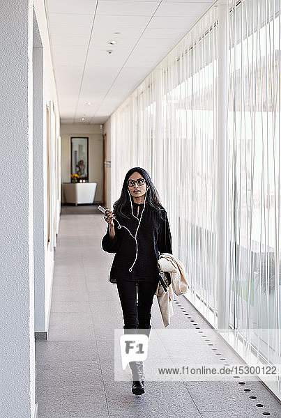 Geschäftsfrau in voller Länge  die im Büro auf dem Flur mit einem Smartphone spricht