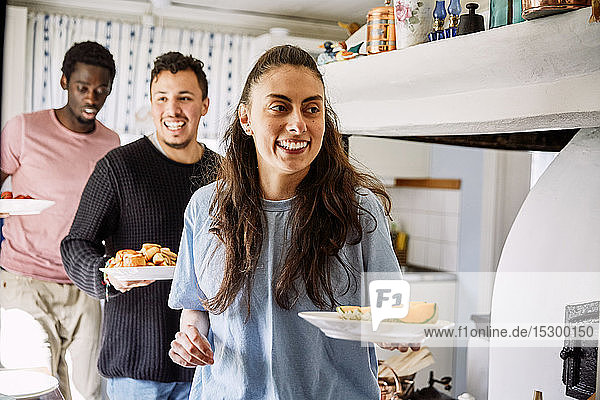 Lächelnde Freunde halten Essen in der Hand  während sie zu Hause in der Küche stehen