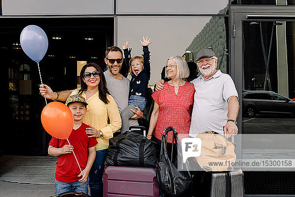 Porträt einer fröhlichen Familie mit Gepäck  die während des Urlaubs am Hoteleingang steht