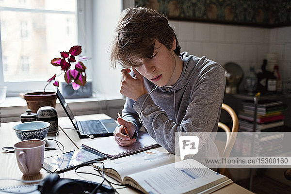 Ernsthafter Teenager liest Buch  während er zu Hause Hausaufgaben macht