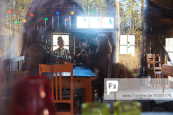 Male and female friends talking while enjoying at table in cottage seen through window