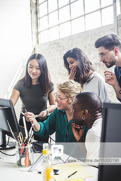 Smiling computer hackers discussing over desktop PC in creative office