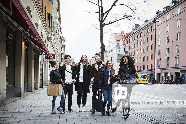 Smiling male and female teenage friends walking on sidewalk in city