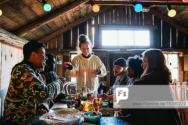 Lächelnde junge Frau unterhält sich beim Essen mit Freunden in einer Hütte