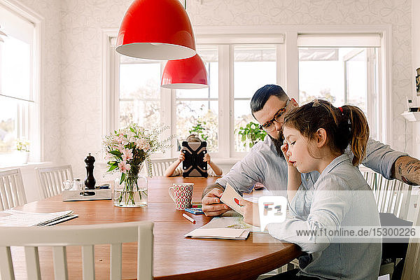 Mann assistiert der Tochter  während das Mädchen das digitale Tablet im Hintergrund zu Hause benutzt