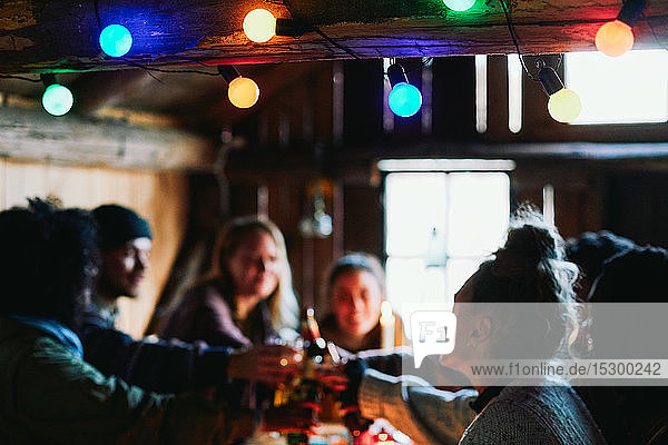 Glücklicher Mann und Freunde stoßen auf Getränke an  während sie in der Hütte sitzen
