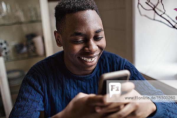 Lächelnder Teenager benutzt Smartphone  während er zu Hause sitzt
