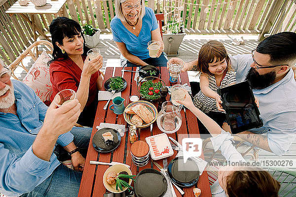 Hochwinkelansicht einer Familie  die auf Trinkgläser anstößt  während sie auf der Terrasse am Tisch sitzt