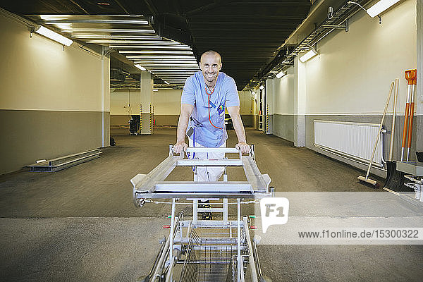 Lächelnder männlicher Arzt steht mit Bahre im Krankenhauskorridor