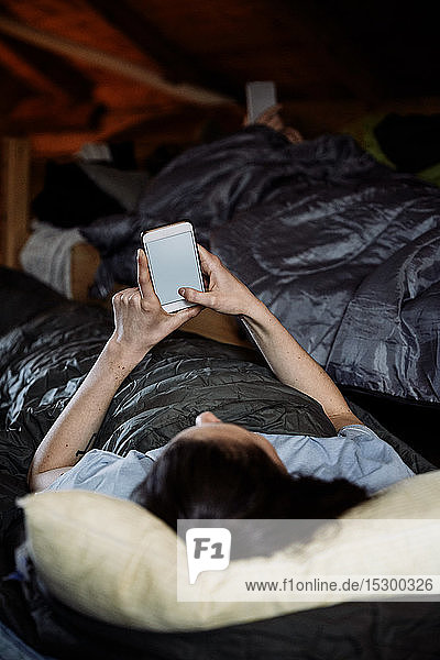 Junge Frau benutzt Smartphone  während sie auf einer Matratze in einem Ferienhaus liegt