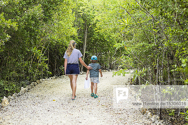 rear view of 13 year old sister and her 5 year old brother walking on nature path