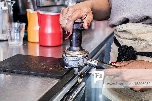 Barista-Frau  die Kaffeebohnen gemahlen zubereitet und sie in einem Café in einen Kaffeesatzhalter stampfte.