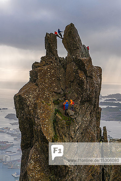 Eine Gruppe von Menschen klettert auf den Svolvï¿½r Ziege  150 Meter (490 ft)  eine zackige Zinne hoch über der Landschaft der Lofoten.
