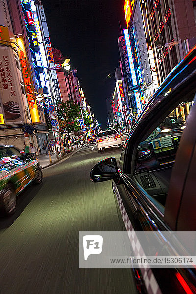 Bewegungsunscharfe Sicht aus dem Taxi auf Straßen- und Neonreklamen in der Nacht im Bezirk Shinjuku  Tokio  Japan.