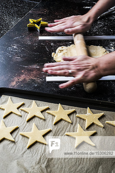 Hochwinkel-Nahaufnahme der Person  die den Teig für sternförmige Kekse ausrollt  unter Verwendung von zwei Führungsstangen  um eine gleichmäßige Teigdicke zu erhalten.