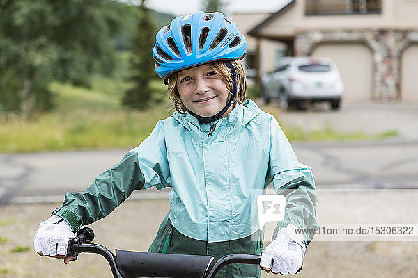 Porträt eines 5-jährigen Jungen in Regenjacke  der auf seinem Fahrrad sitzt