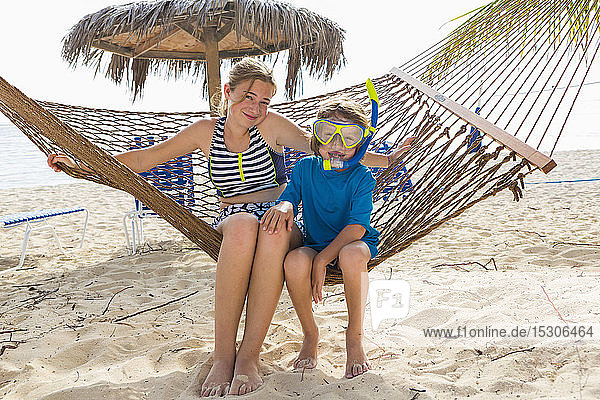 A teenage girl and her brother sitting on a hammock on the beach.
