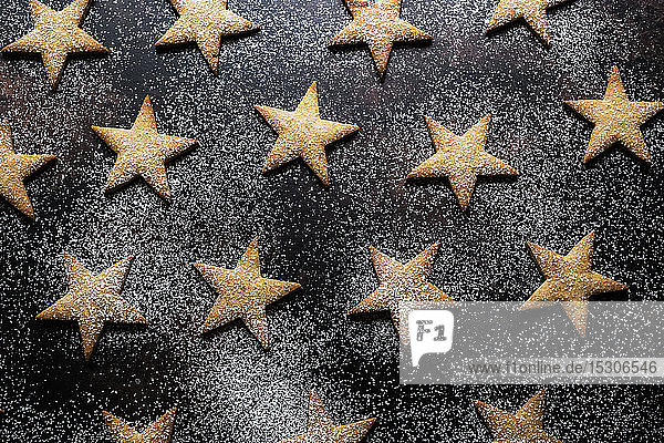 Hochwinkel-Nahaufnahme von frisch gebackenem  mit Puderzucker bestäubtem Sternengebäck auf schwarzem Hintergrund.