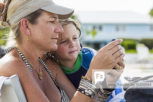 Mutter und 5 Jahre alter Sohn schauen sich am Strand ein Smartphone an