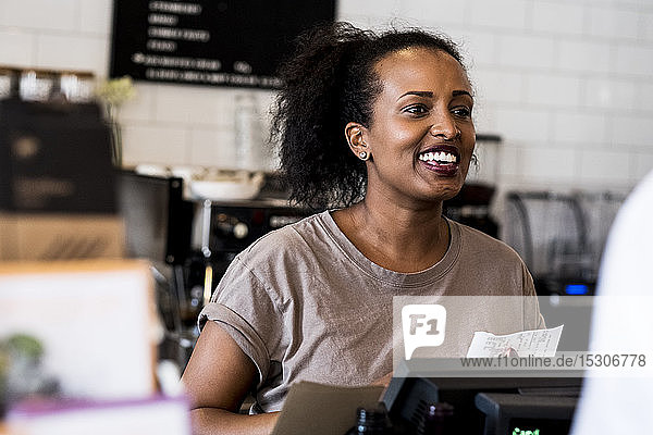 A woman barista smiling in welcome beside the counter in a coffee shop.