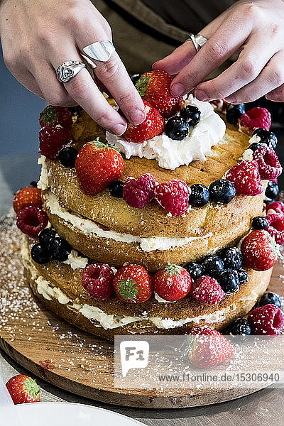 A woman cook assembling a layer cake with fresh cream and fresh fruit  strawberries and blueberries.