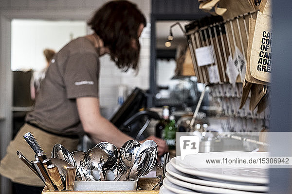 Nahaufnahme eines Stapels von Tellern und Behältern mit Besteck in einem Restaurant  Frau arbeitet im Hintergrund.
